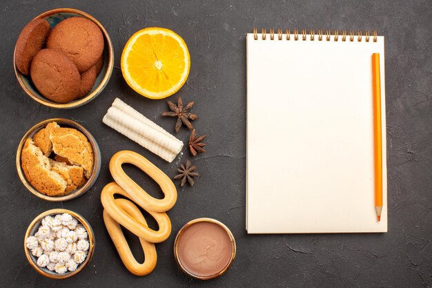 Top view delicious cookies with fresh oranges on dark surface cookies biscuit sugar cake dessert sweet