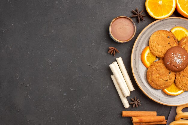 Вид сверху вкусного печенья со свежими нарезанными апельсинами на темном фоне сахарное печенье фруктовое печенье сладкое