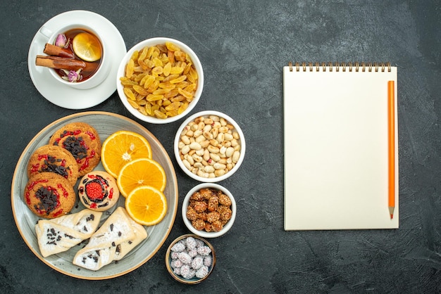 Top view delicious cookies with fruity pastries orange tea and nuts on a dark surface nut snack tea sweet candy