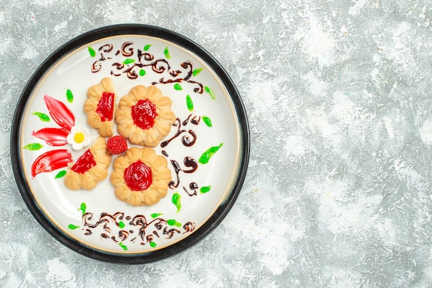 Top view delicious cookies with red jelly inside plate on white background cake cookies sweet tea