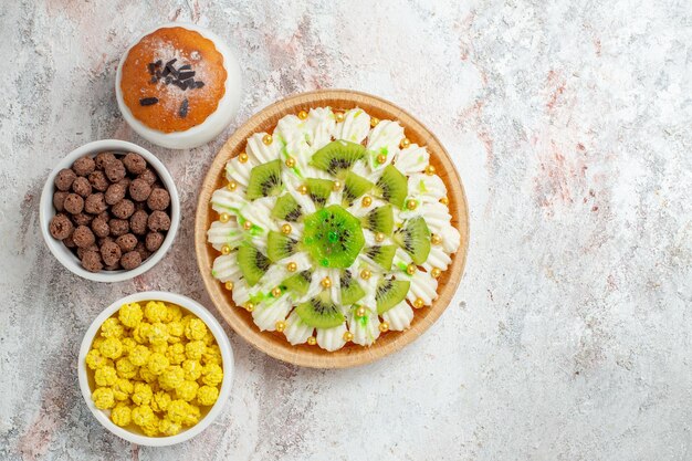 Top view delicious cream dessert with white cream and sliced kiwis on white desk candy biscuit cream cake dessert