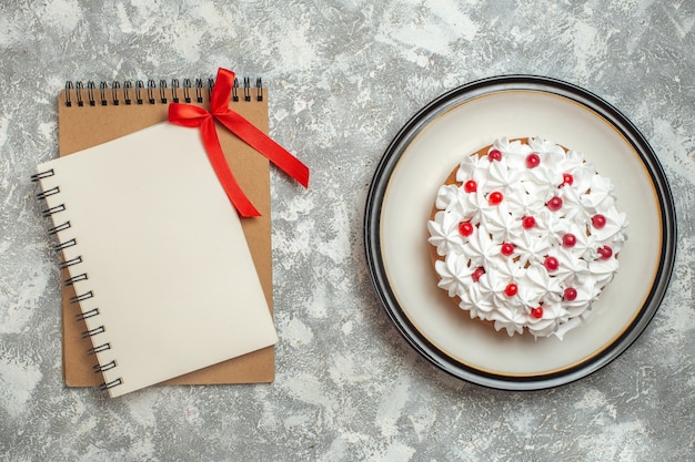 Top view of delicious creamy cake decorated with fruits and notebooks on ice background