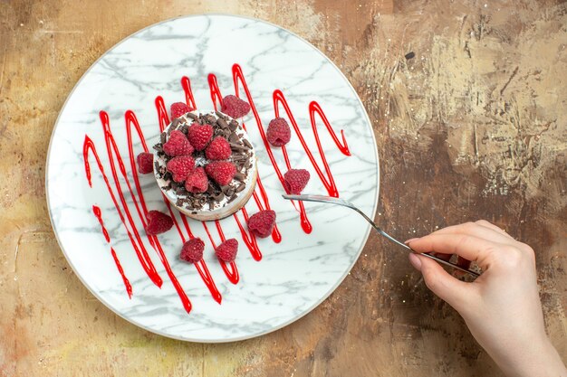 갈색 배경에 라스베리가 있는 접시 안에 있는 맛있는 크림 케이크