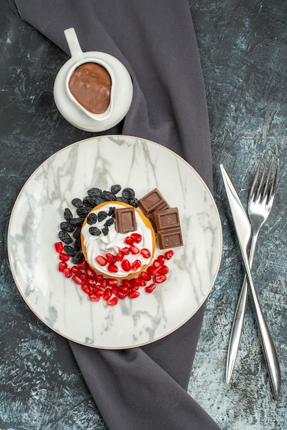 Top view delicious creamy cake with chocolate and raisins on light-dark background