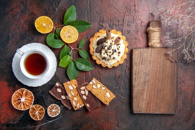 Top view delicious creamy cake with cup of tea on dark floor sweet cake dessert