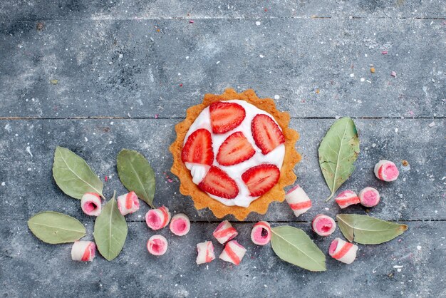 top view of delicious creamy cake with sliced fresh strawberries and sliced pink candies on grey, cake sweet bake cream fruit candy