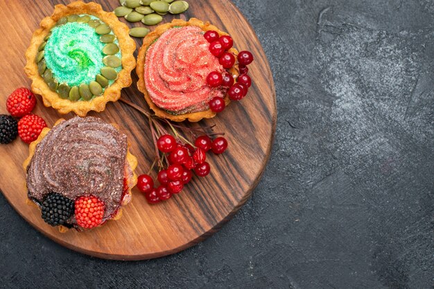 Вид сверху вкусные сливочные пирожные с ягодами на темном столе, печенье, печенье