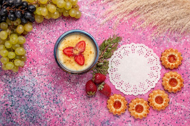 Вид сверху вкусный сливочный десерт со свежим зеленым виноградом и печеньем на светло-розовом фоне десертное мороженое ягодный крем сладкие фрукты