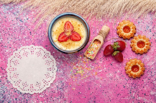 Вид сверху вкусный сливочный десерт с красной нарезанной клубникой и маленьким печеньем на светло-розовом фоне десертное мороженое ягодный крем сладкие фрукты