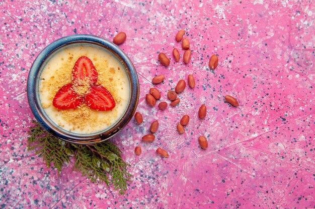 Top view delicious creamy dessert with red sliced strawberries and nuts on light pink background dessert ice-cream cream color sweet fruit berry