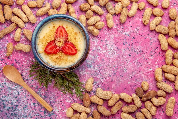 Top view delicious creamy dessert with red sliced strawberries and peanuts on light pink desk dessert ice-cream cream color sweet fruits berry