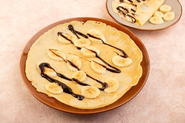 A top view delicious dessert slice designed with chocolate inside brown round plate on the pink desk food meal dessert pastry