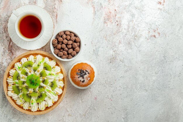 Top view delicious dessert with sliced kiwis and cup of tea on white background biscuit cream fruit dessert candy cake