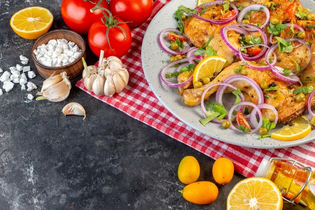 濃い色の背景の左側に茎ニンニク落ちたオイルボトルとさまざまなスパイスと食品トマトとおいしい夕食フライドチキン料理の上面図