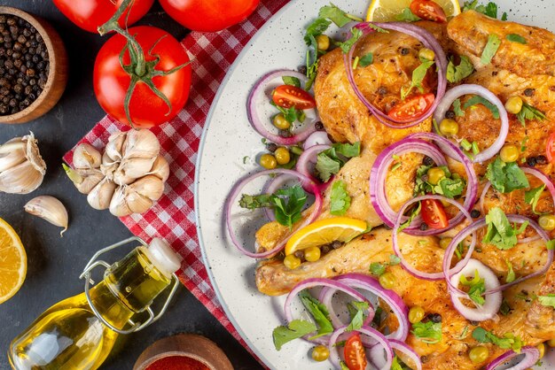 Top view of delicious dinner fried chicken dish with various spices and foods tomatoes with stems pepper onions garlics fallen oil bottle on dark color background