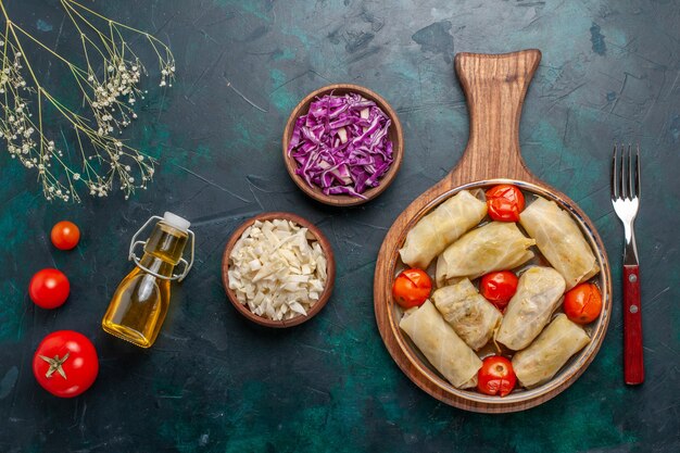 Top view delicious dolma meat meal rolled with cabbage and tomatoes along with oil on dark-blue desk meat food dinner vegetables dish cooking