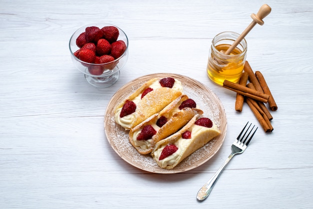 Free photo a top view delicious eclairs with cream and strawberries along with cinnamon and honey on the white background  cake fruit