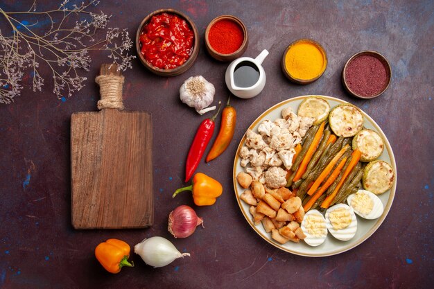 Top view delicious egg meal with cooked vegetables and seasonings on a dark space