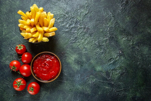 Vista dall'alto deliziose patatine fritte con pomodorini sulla superficie scura