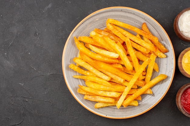 Foto gratuita vista dall'alto deliziose patatine fritte con condimenti sul piatto di fast-food di hamburger di pasto di patate sfondo scuro