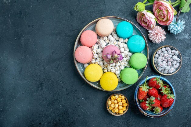 Top view delicious french macarons with candies inside tray on a dark space