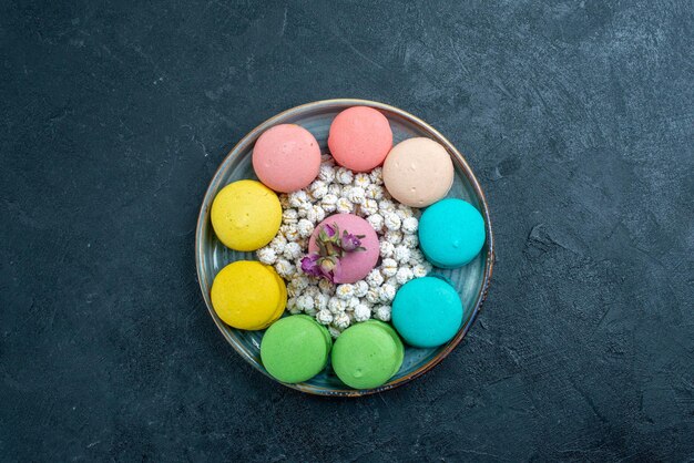 Top view delicious french macarons with candies inside tray on dark space