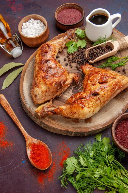 Вид сверху вкусной жареной курицы с разными приправами на темном столе