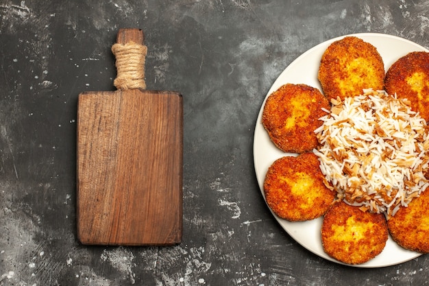 Foto gratuita vista dall'alto deliziose cotolette fritte con riso cotto su foto di piatto di carne superficie scura