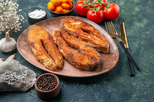 Вид сверху вкусной жареной рыбы на коричневой тарелке и набор столовых приборов, специи, продукты на столе смешанных цветов со свободным пространством