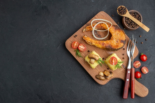 나무 커팅 보드 칼 붙이에 맛있는 튀긴 생선과 버섯 토마토 채소의 상위 뷰 검은 표면에 고추를 설정