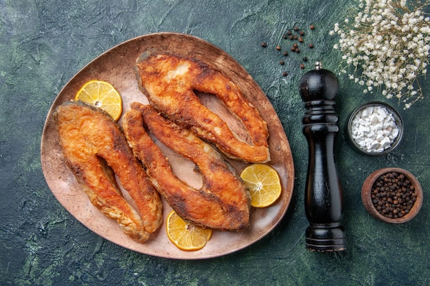 Top view of delicious fried fishes and lemon slices on a brown plate spices on mix colors table with free space