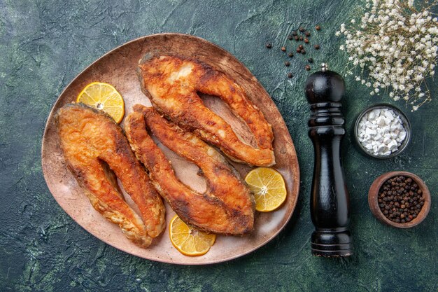 Вид сверху вкусной жареной рыбы и ломтиков лимона на коричневой тарелке со специями на столе смешанных цветов со свободным пространством