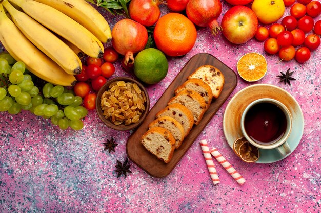 Вид сверху вкусной фруктовой композиции с нарезанными тортами и чашкой чая на розовом столе