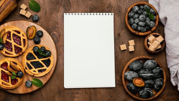 Top view of delicious fruit pies with plums and notebook