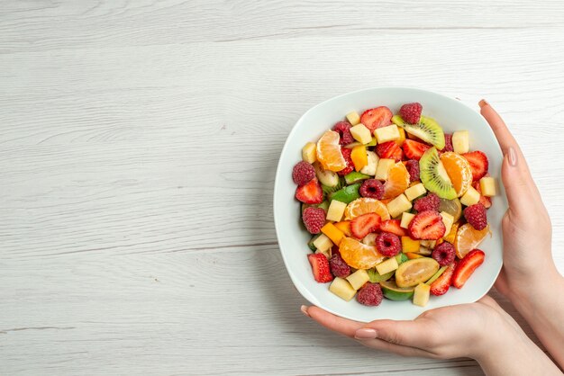 Вид сверху вкусный фруктовый салат нарезанные фрукты внутри тарелки на белом цвете здоровый образ жизни фото фрукты спелые спелые