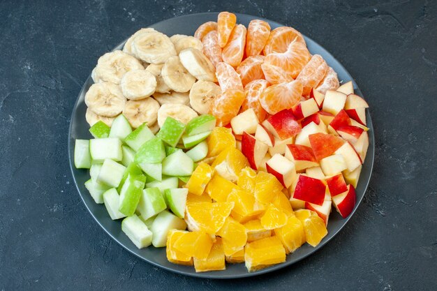 Top view delicious fruit salad sliced tangerines apples bananas and oranges on dark background