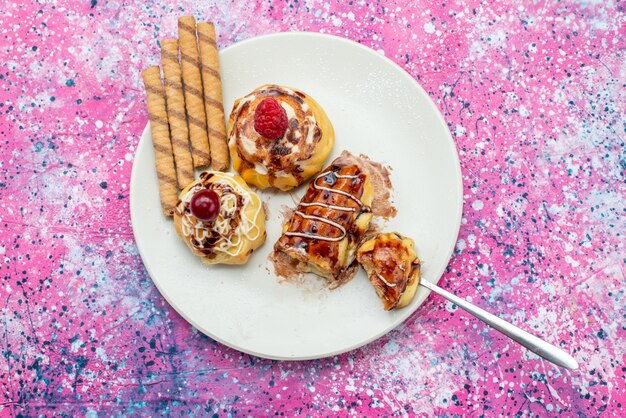 ピンクのデスクケーキビスケットの甘い焼く上の白いプレート内のクリームとチョコレートのおいしいフルーティーなケーキのトップビュー