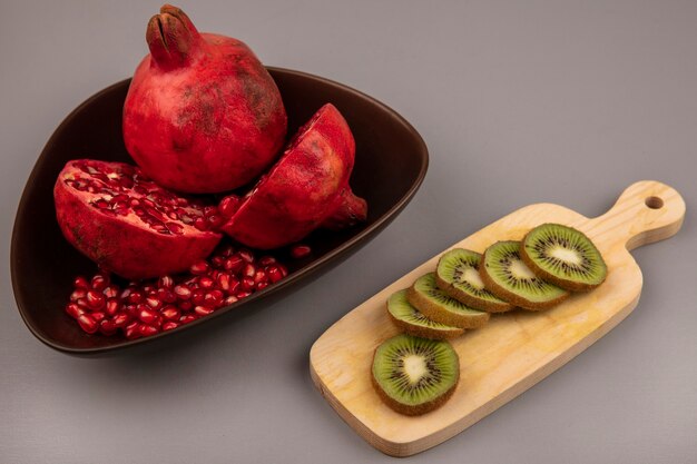 Top view of delicious halved and whole pomegranates on a bowl with slices of kiwi on a wooden kitchen board