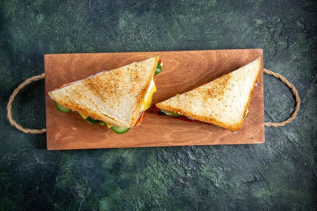 Top view delicious ham sandwiches on wooden board dark surface