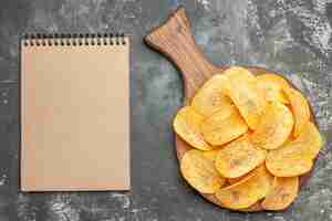 Free photo top view of delicious homemade chips on wooden cutting board and notebook on gray background