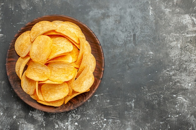 Top view of delicious homemade potato chips on a brown plate on gray background