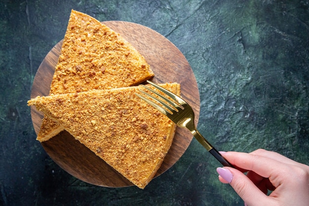 Top view delicious honey cake slice of it on round wooden board dark surface