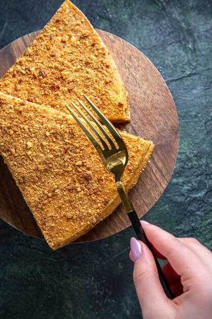 Top view delicious honey cake slice of it on round wooden board dark surface