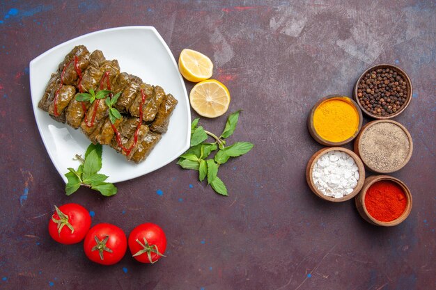 Вид сверху вкусной листовой долмы с лимонными приправами и помидорами на темном столе, блюдо, ужин, еда, мясо