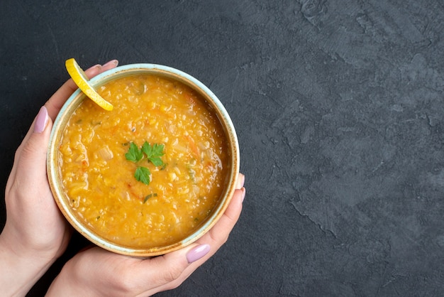 Vista dall'alto deliziosa zuppa di lenticchie con piatto di tenuta femminile sulla superficie scura