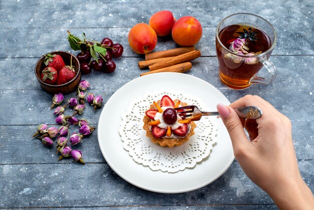 Вид сверху восхитительный торт со сливками и свежими нарезанными фруктами вместе с чаем с корицей на серо-синем столе фруктовый торт бисквитный чай сахар