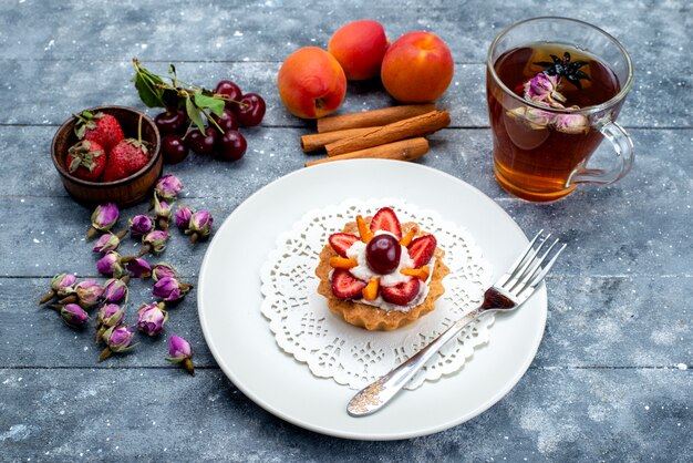 Вид сверху восхитительного маленького пирога со сливками и свежими нарезанными фруктами вместе с чаем с корицей на серо-синем бисквите фруктового торта на столе