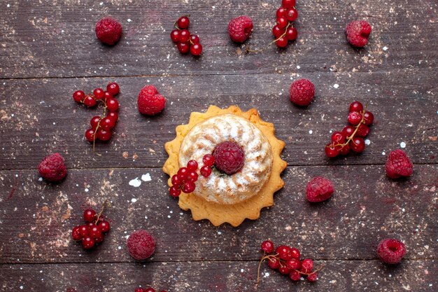 Top view of delicious little cake with sugar powder along with raspberries cranberries all along brown desk, berry fruit cake biscuit