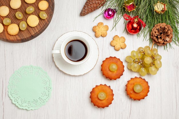 Top view delicious little cakes with grapes and cup of tea on light white desk pie cake tea biscuit cookie