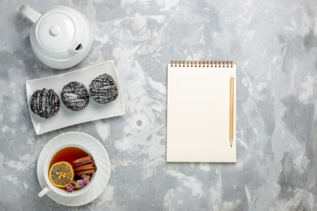 Top view delicious little cakes with icing and cup of tea on white background tea biscuit cake bake sugar sweet pie cookies